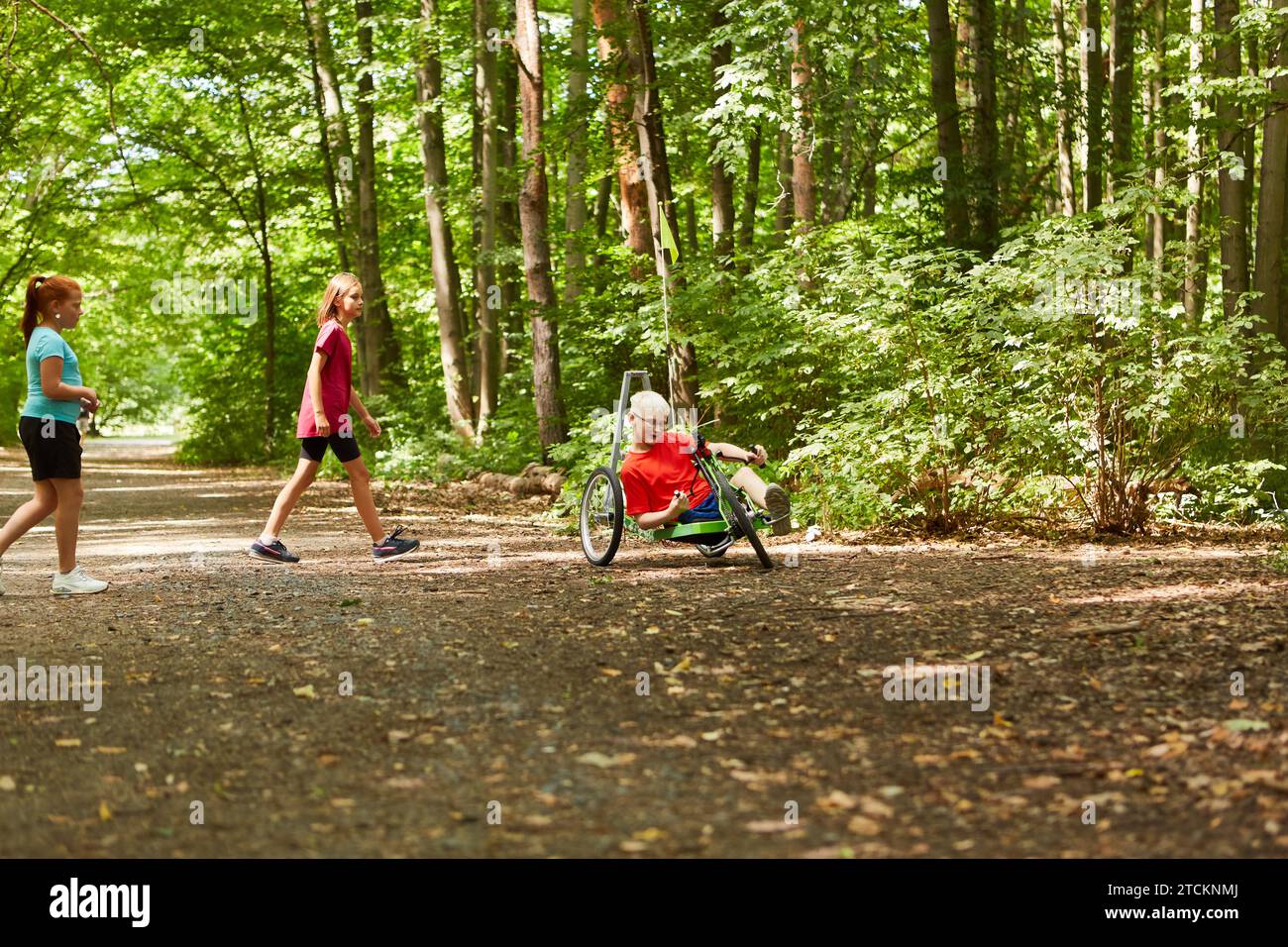 Amici che giocano con un ragazzo handicappato in bicicletta reclinata su un sentiero nella foresta Foto Stock