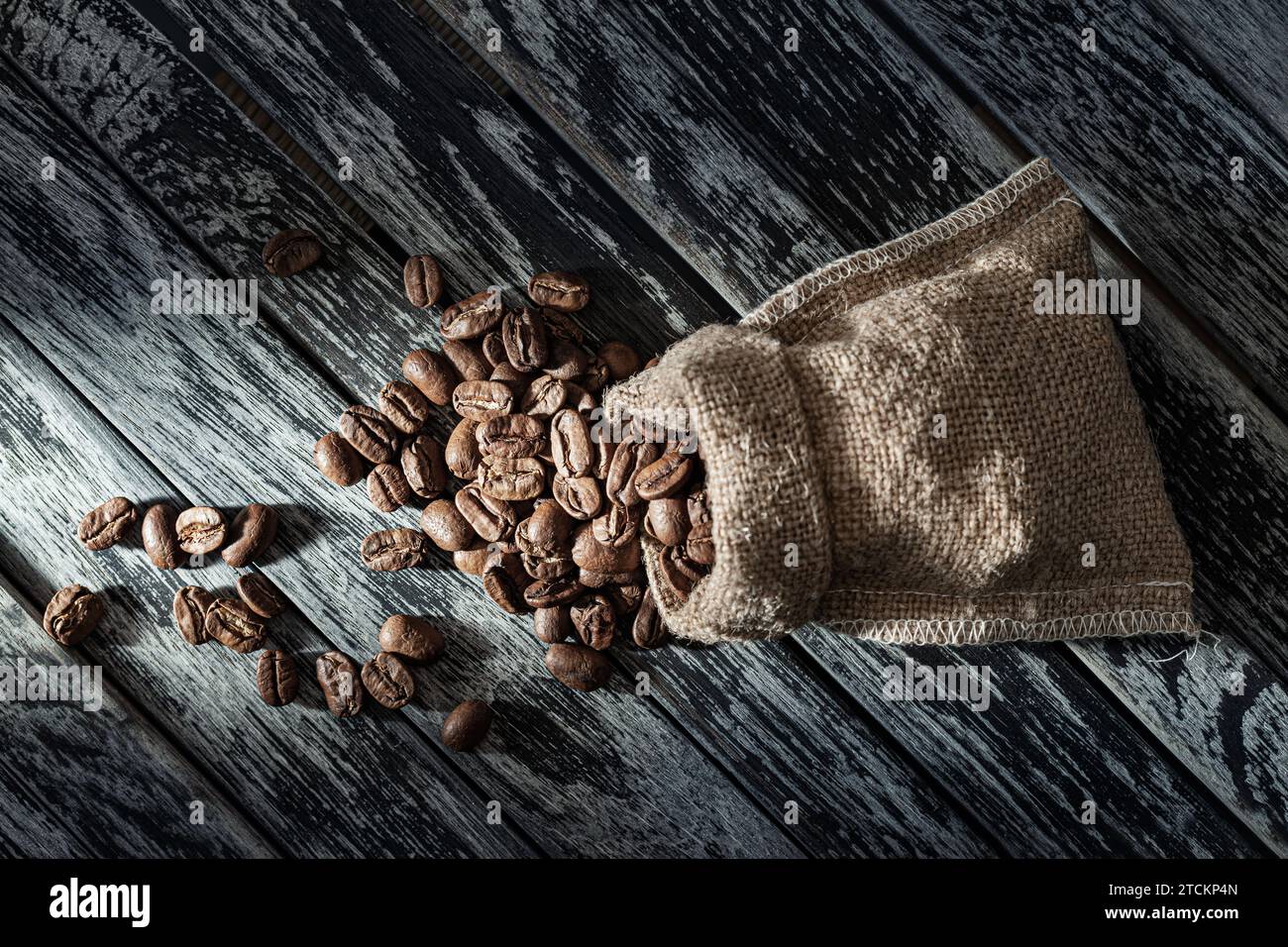 Chicchi di caffè versati da Burlap Sack su Wintage Wood Foto Stock