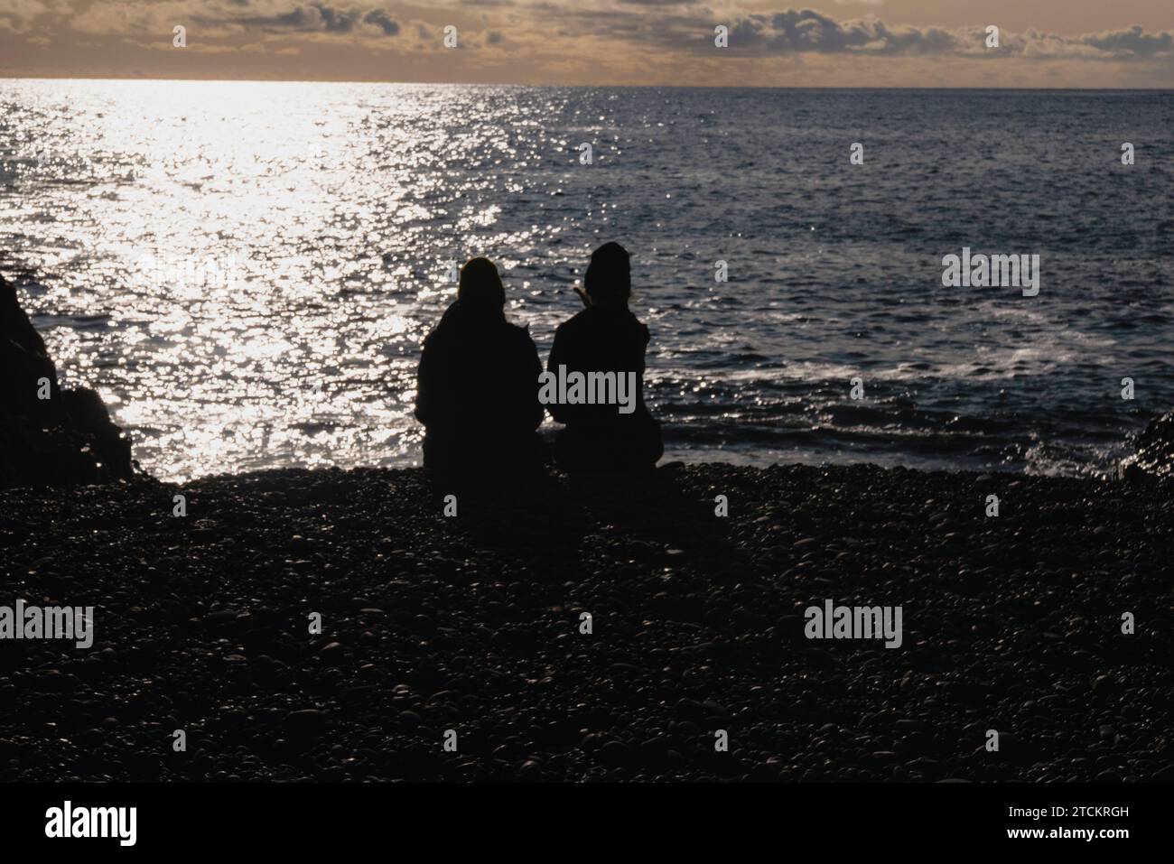 Islanda, Parco nazionale della penisola di Snæfellsnes, spiaggia di sabbia nera di Djúpalónssandur. Due persone in silhouette sedute sulla spiaggia che guardano fuori. Foto Stock