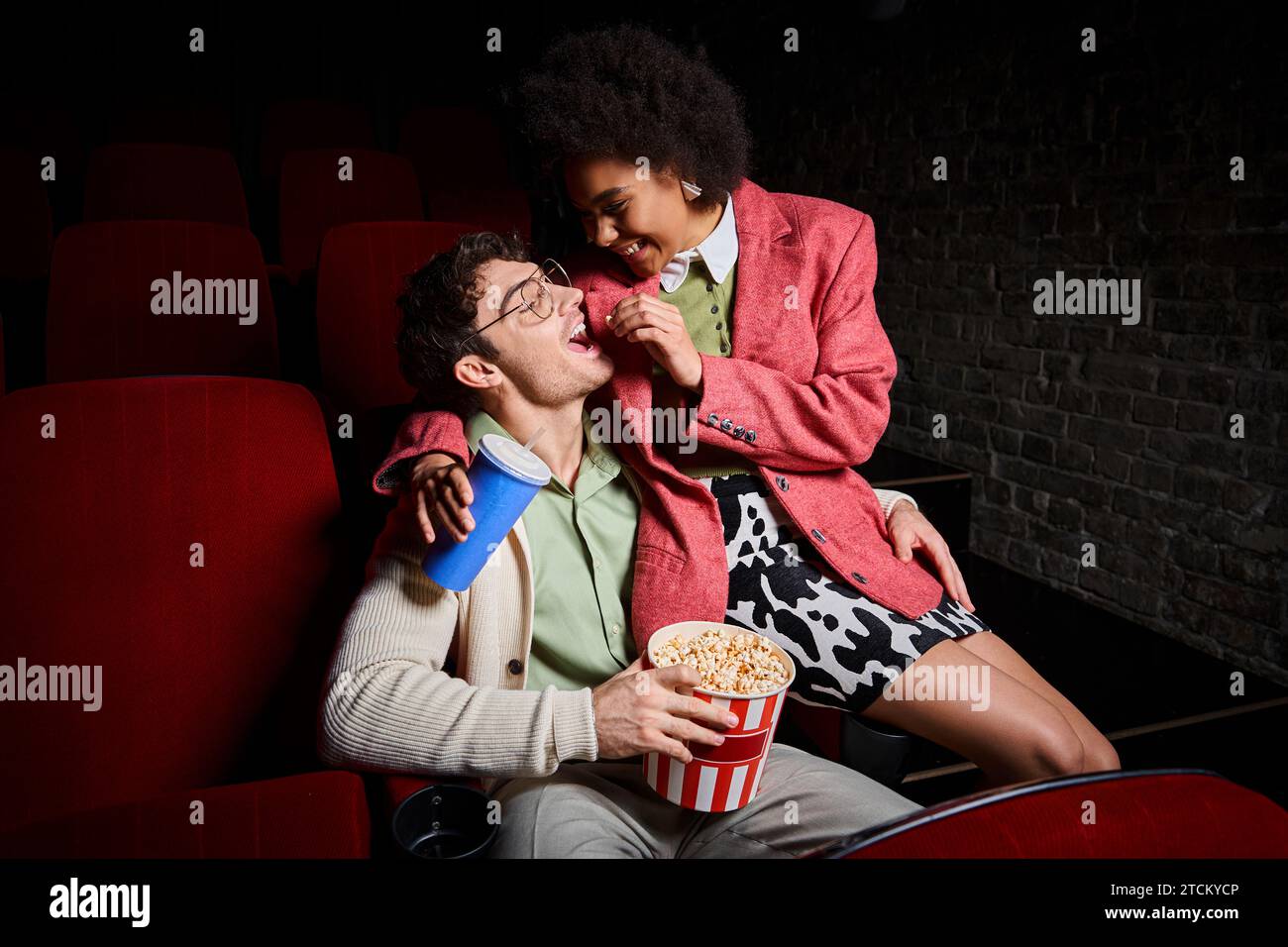 allegra donna afro-americana che condivide popcorn con il suo ragazzo mentre è seduta sui suoi giri Foto Stock