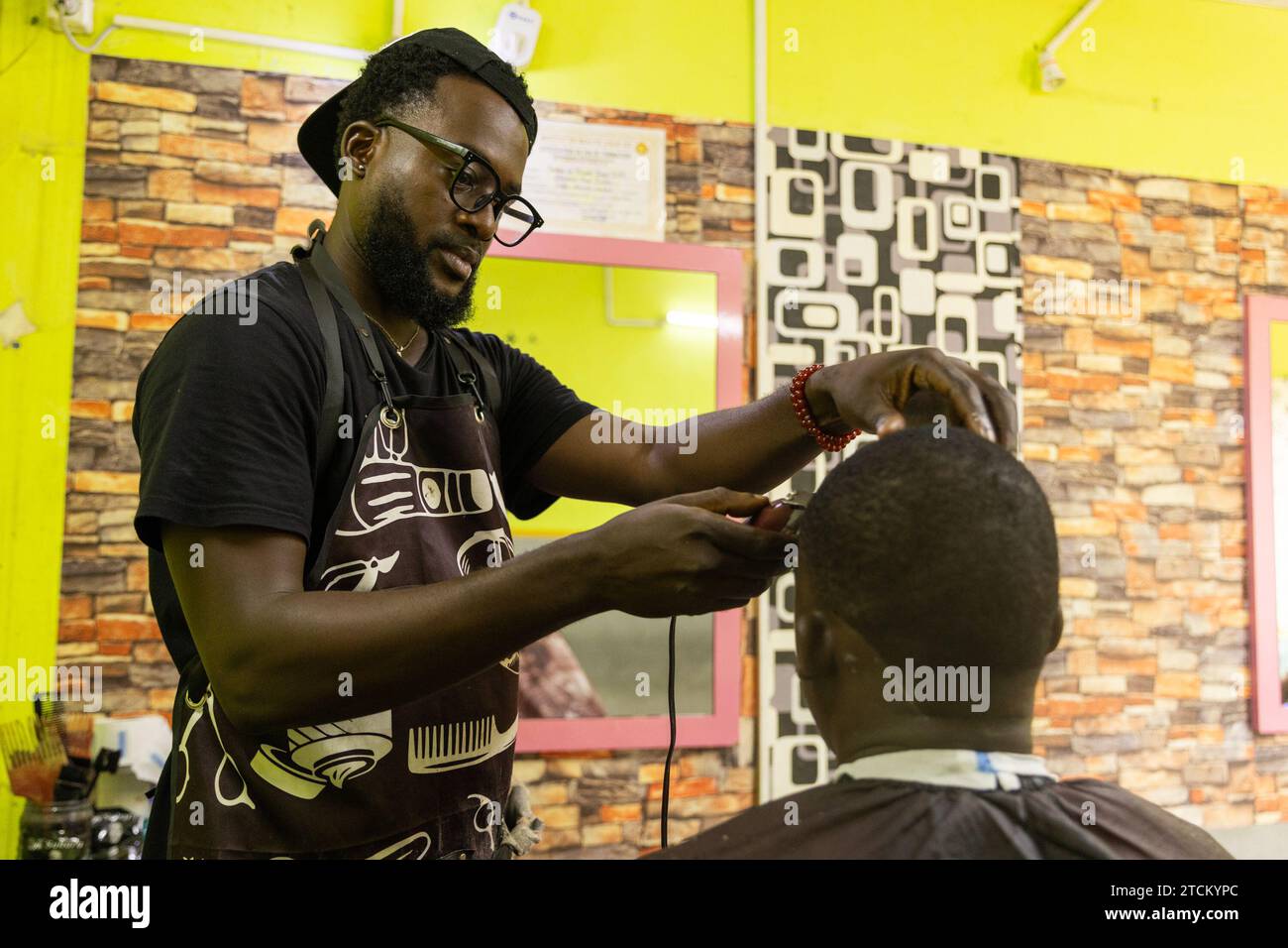 Un barbiere si concentra sul taglio dei capelli del suo cliente nel suo salone. Foto Stock