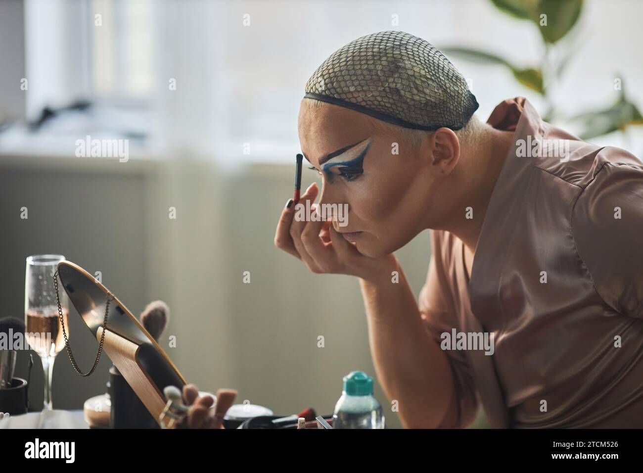 Ritratto laterale di drag queen che esegue il trucco del palcoscenico e guarda a specchio, spazio di copia Foto Stock