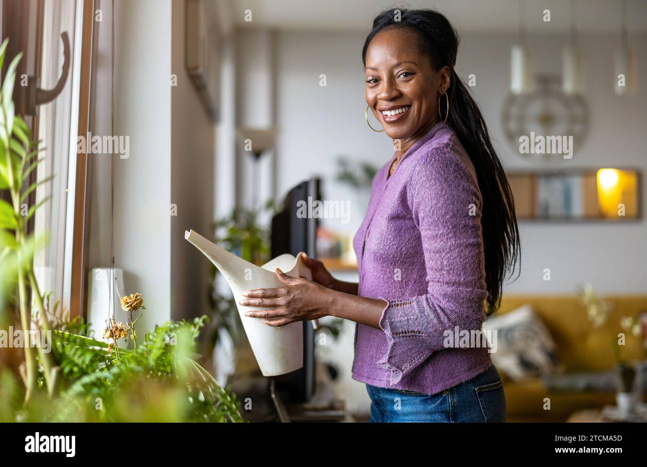 Bella donna che annaffia le piante a casa Foto Stock