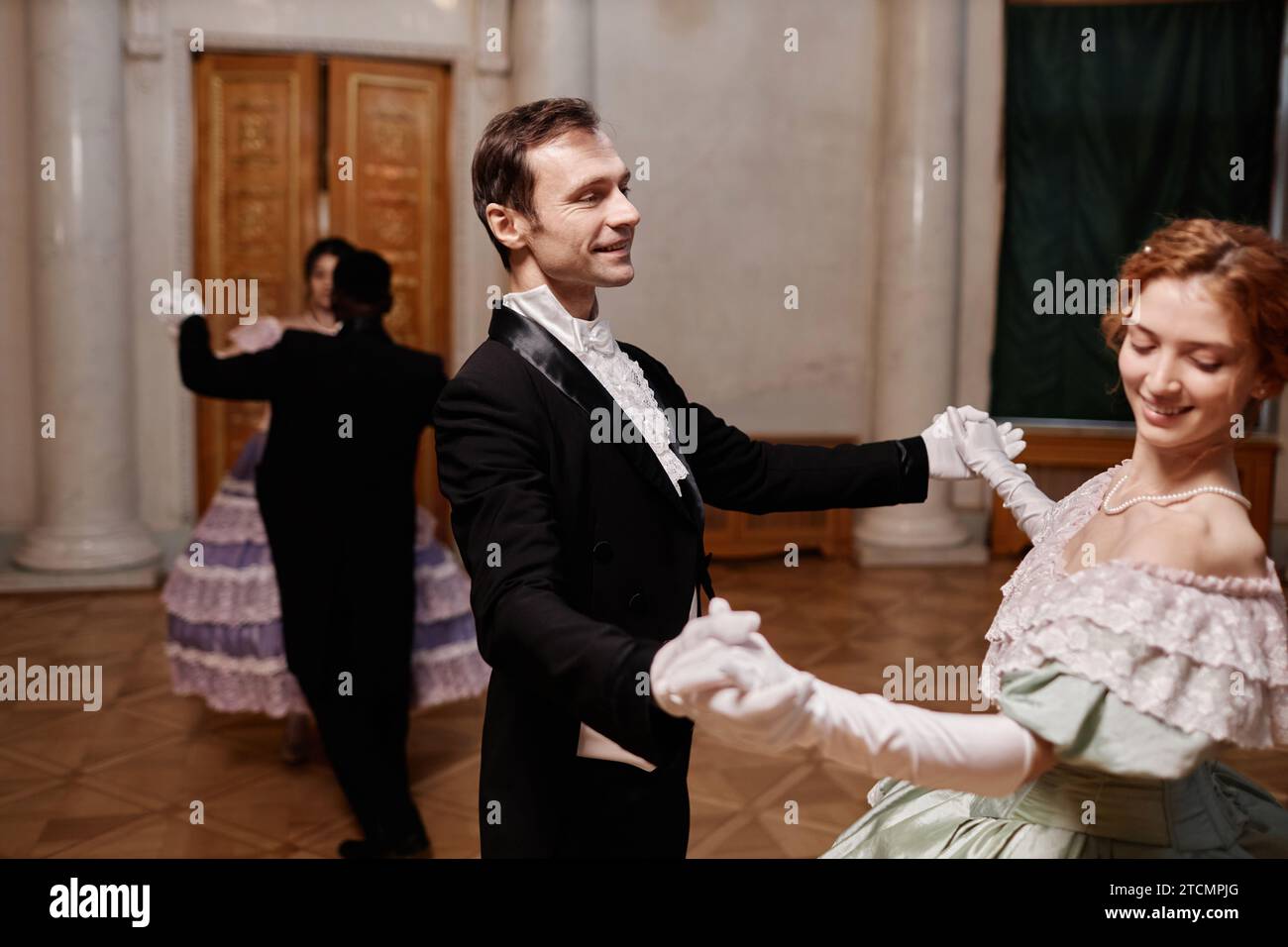 Ritratto di un gentiluomo sorridente che indossa un classico tailcoat che balla con la giovane donna durante il ballo di debutto nel palazzo, spazio copia Foto Stock