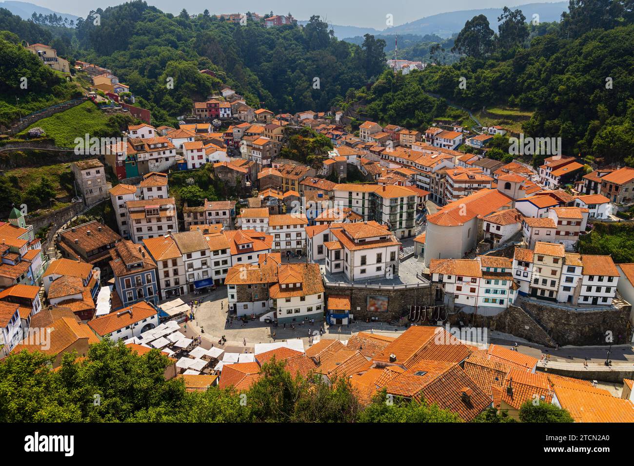 Piccolo villaggio costiero di pescatori con case bianche e tetti rossi, circondato da colline ricoperte di verdi alberi decidui. Cudillero, Asturie, Spagna Foto Stock
