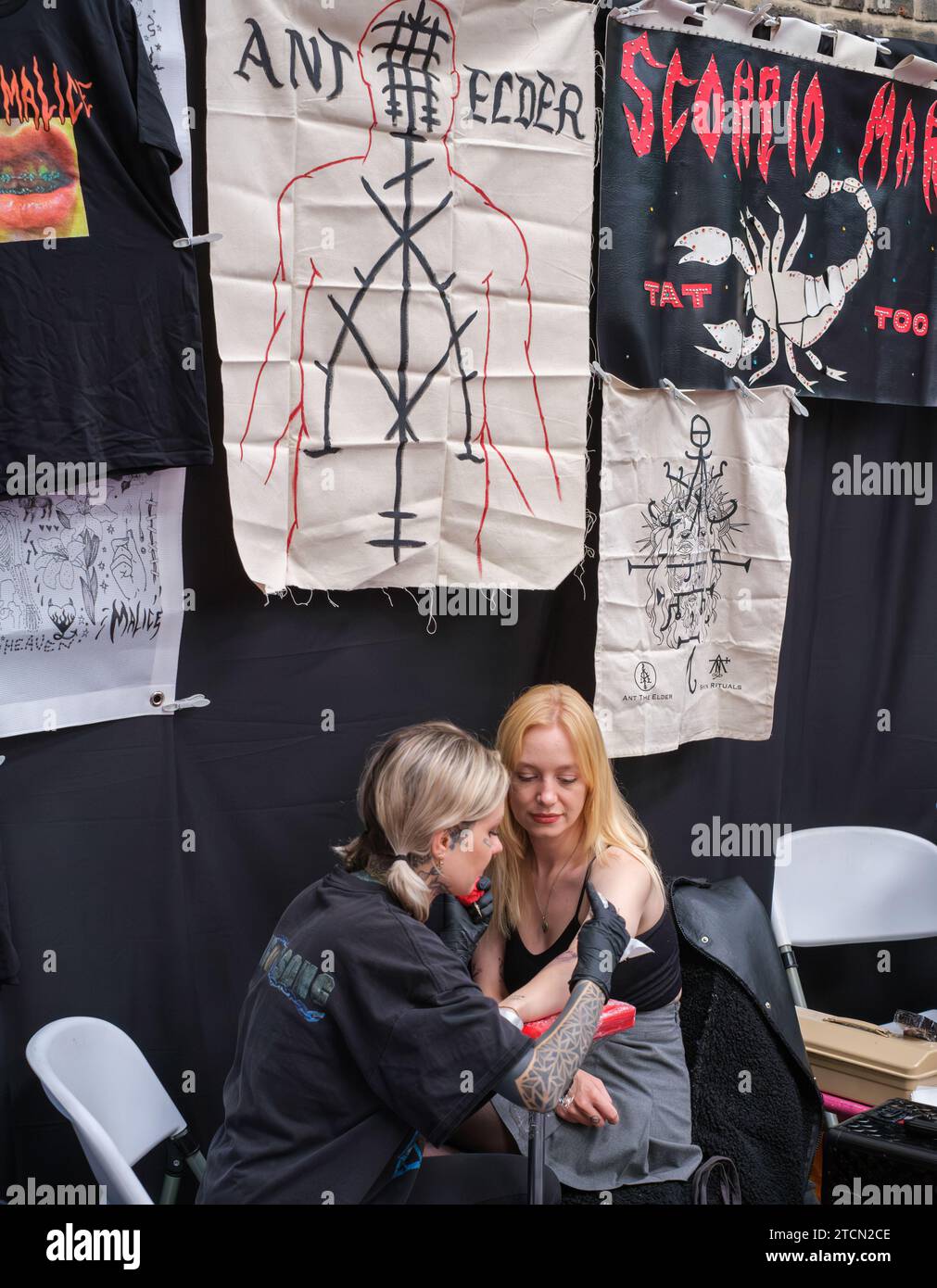 Una giovane donna siede mentre un tatuaggio è inciso sulla parte superiore del braccio durante l'annuale festival del tatuaggio. Foto Stock Una giovane donna siede mentre un tatuaggio è inciso sulla parte superiore del braccio durante l'annuale festival del tatuaggio. Foto Stock