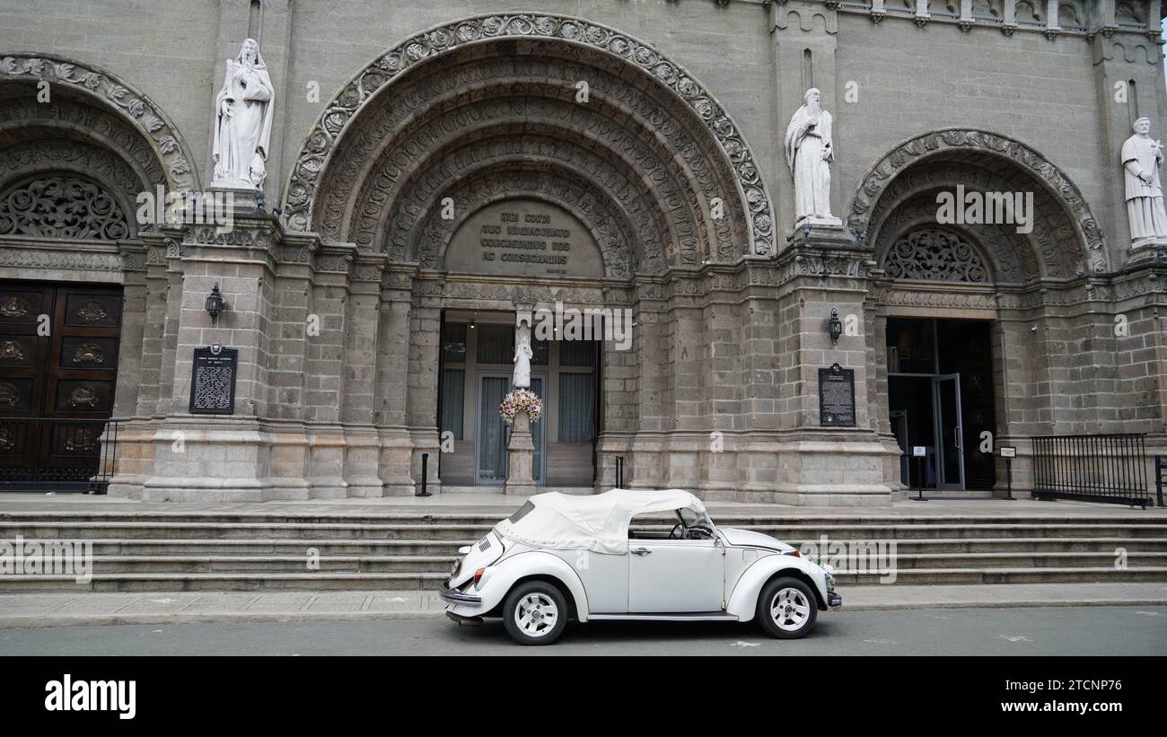 Vista frontale di una chiesa di Intramuros, una città murata creata durante la colonizzazione spagnola a Manila, Filippine, con un'auto bianca parcheggiata di fronte. Foto Stock