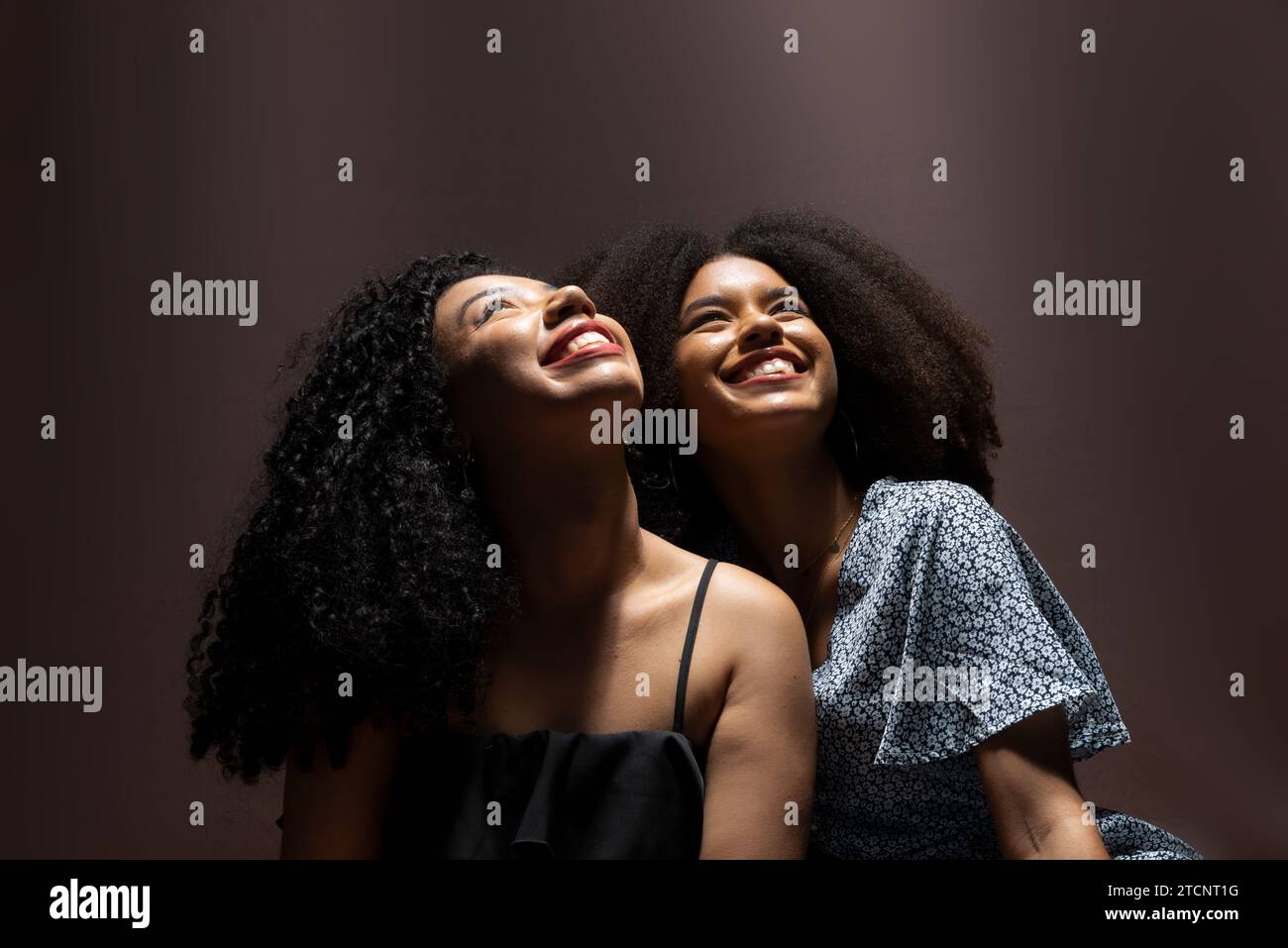 Ritratto di due giovani e bellissimi amici seduti a guardare in alto sorridendo. Studio con scarsa illuminazione. Solido concetto di amicizia. Foto Stock