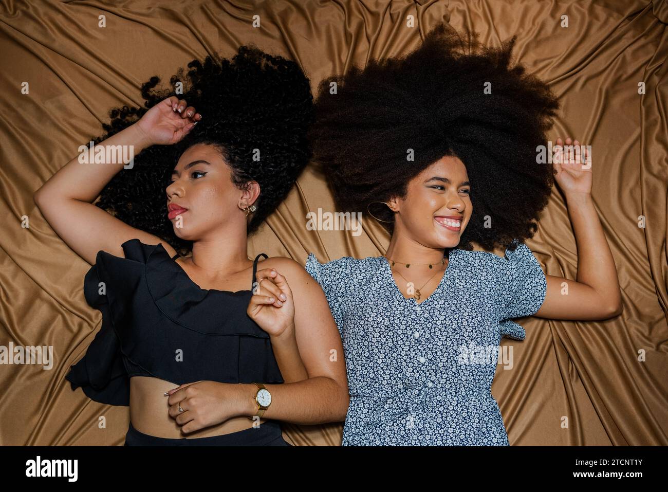 Ritratto a semicerchio di due donne sdraiate con i capelli ricci e la potenza spalmata sul panno per pavimento. Solido concetto di amicizia. Foto Stock