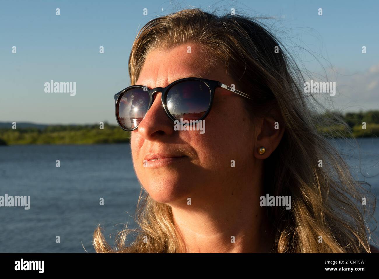 Ritratto di una bella donna bionda che indossa occhiali da sole contro un fiume. Foto Stock