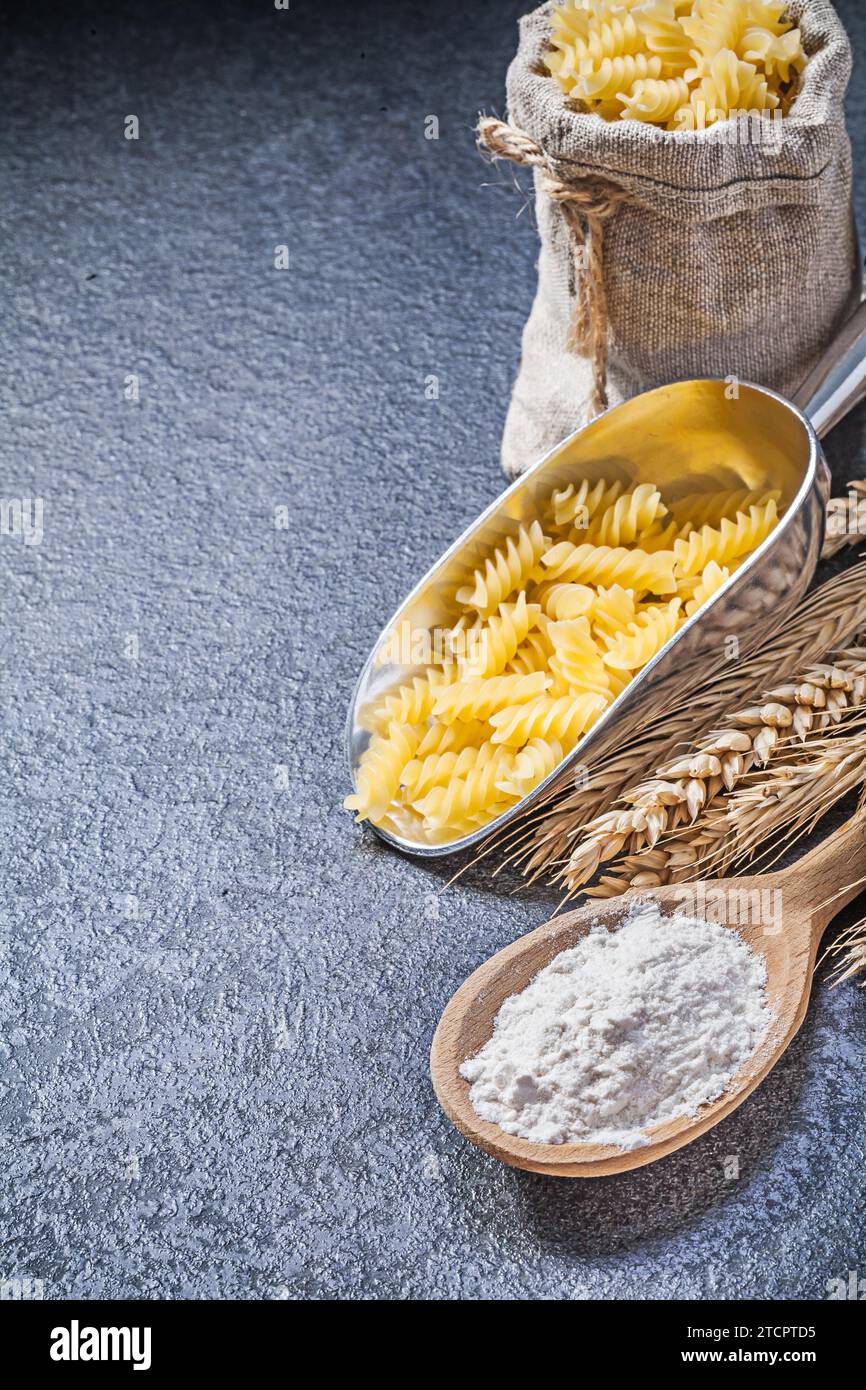 Sacco di rapa che serve pasta cruda, cucchiaio di legno, spighe di segale di grano su fondo nero Foto Stock