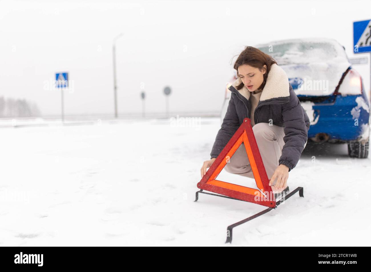 La donna mette un triangolo d'allarme su una strada innevata in inverno, un guasto alle auto in inverno Foto Stock