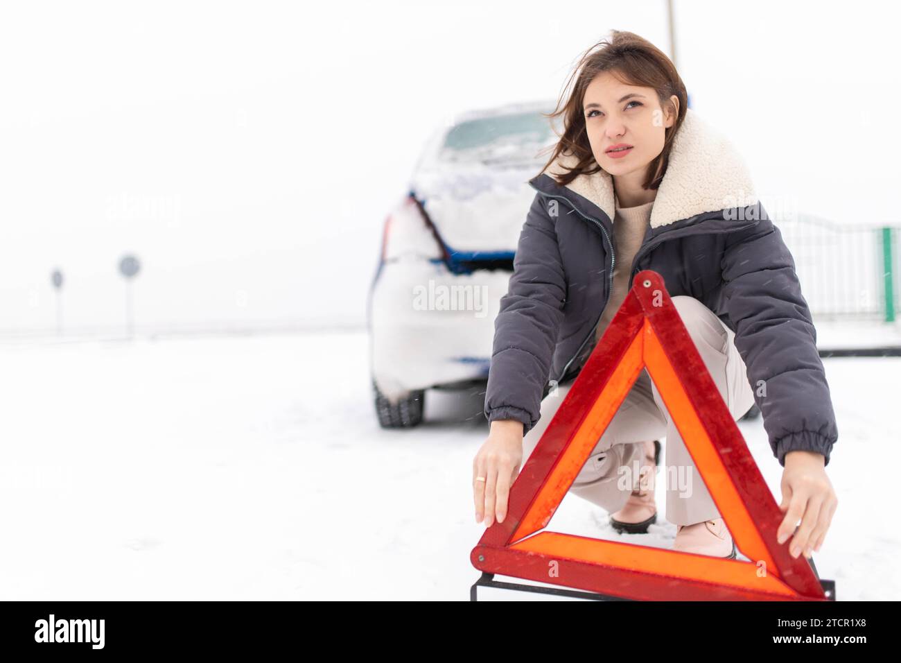 La donna mette un triangolo d'allarme su una strada innevata in inverno, un guasto alle auto in inverno Foto Stock