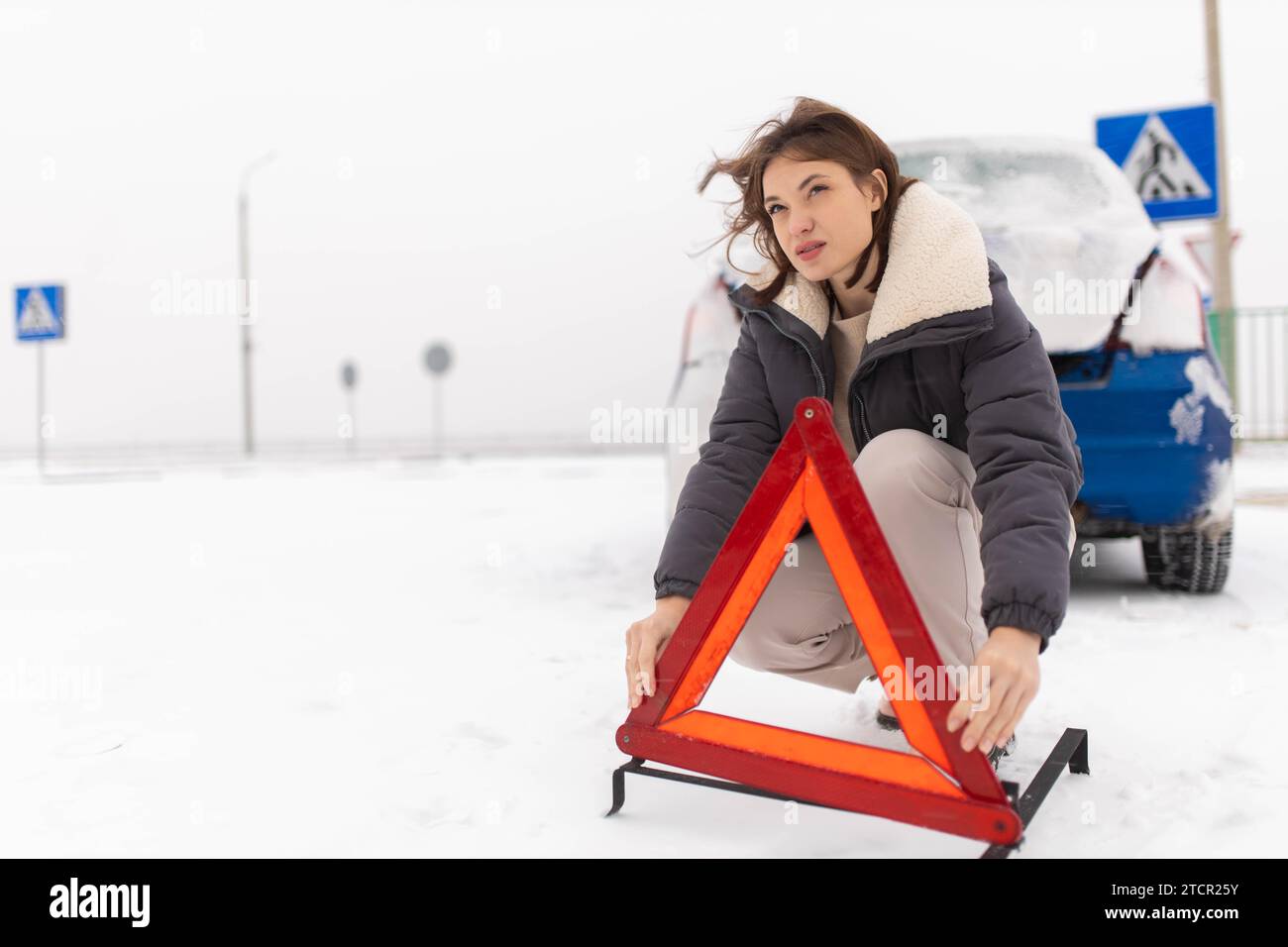 La donna mette un triangolo d'allarme su una strada innevata in inverno, un guasto alle auto in inverno Foto Stock