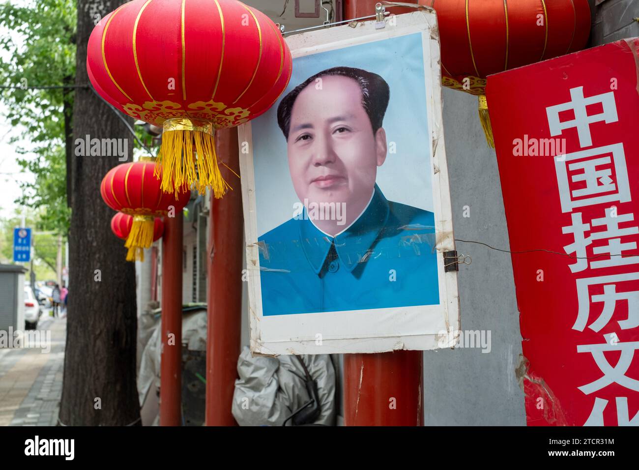 Un ritratto di Mao Zedong e lanterne rosse è appeso di fronte a un negozio che vende vecchi calendari da parete a Pechino, in Cina. 17 aprile 2023 Foto Stock