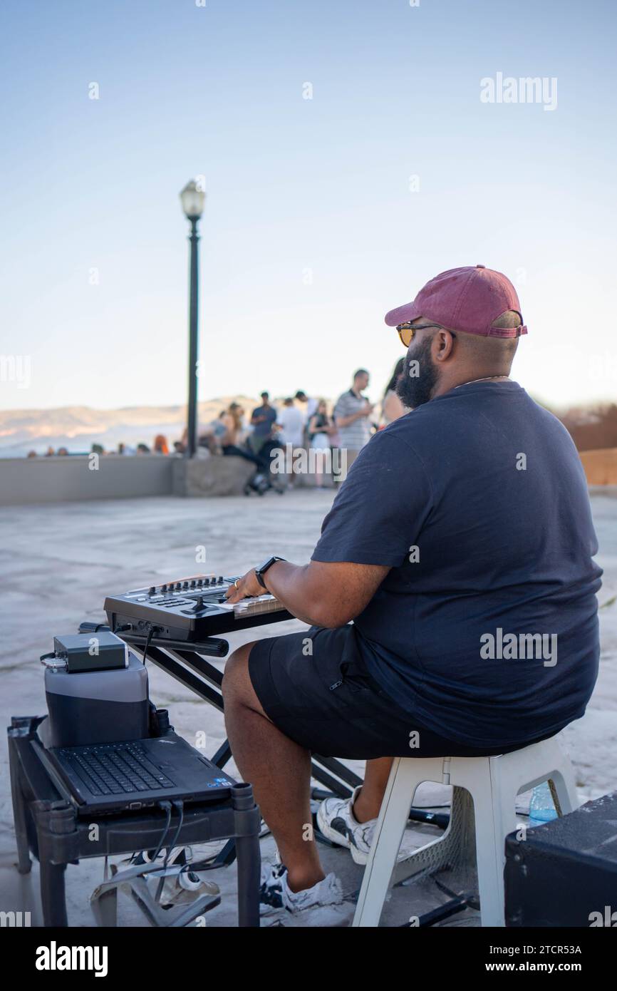 A Serene Sunset Serenade: Un musicista solo maschio sul tetto che suona musica con una tastiera Foto Stock