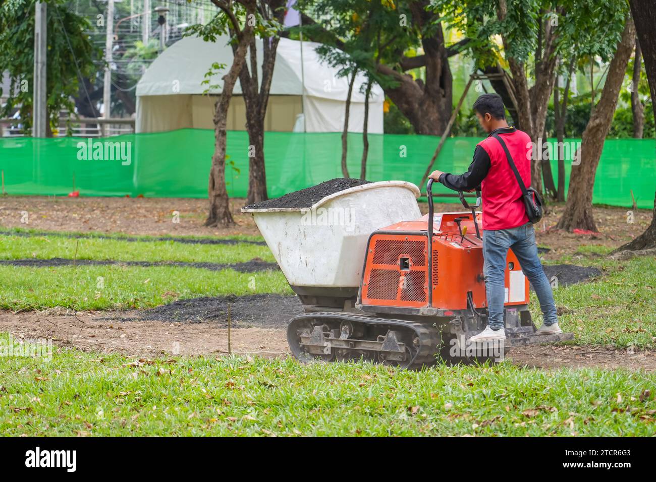 Il lavoratore utilizza attrezzature speciali e trasporta il terreno per la semina nella minipala posteriore su cingoli. Dumper per impieghi gravosi per applicazioni gravose per la costruzione di detriti ro Foto Stock