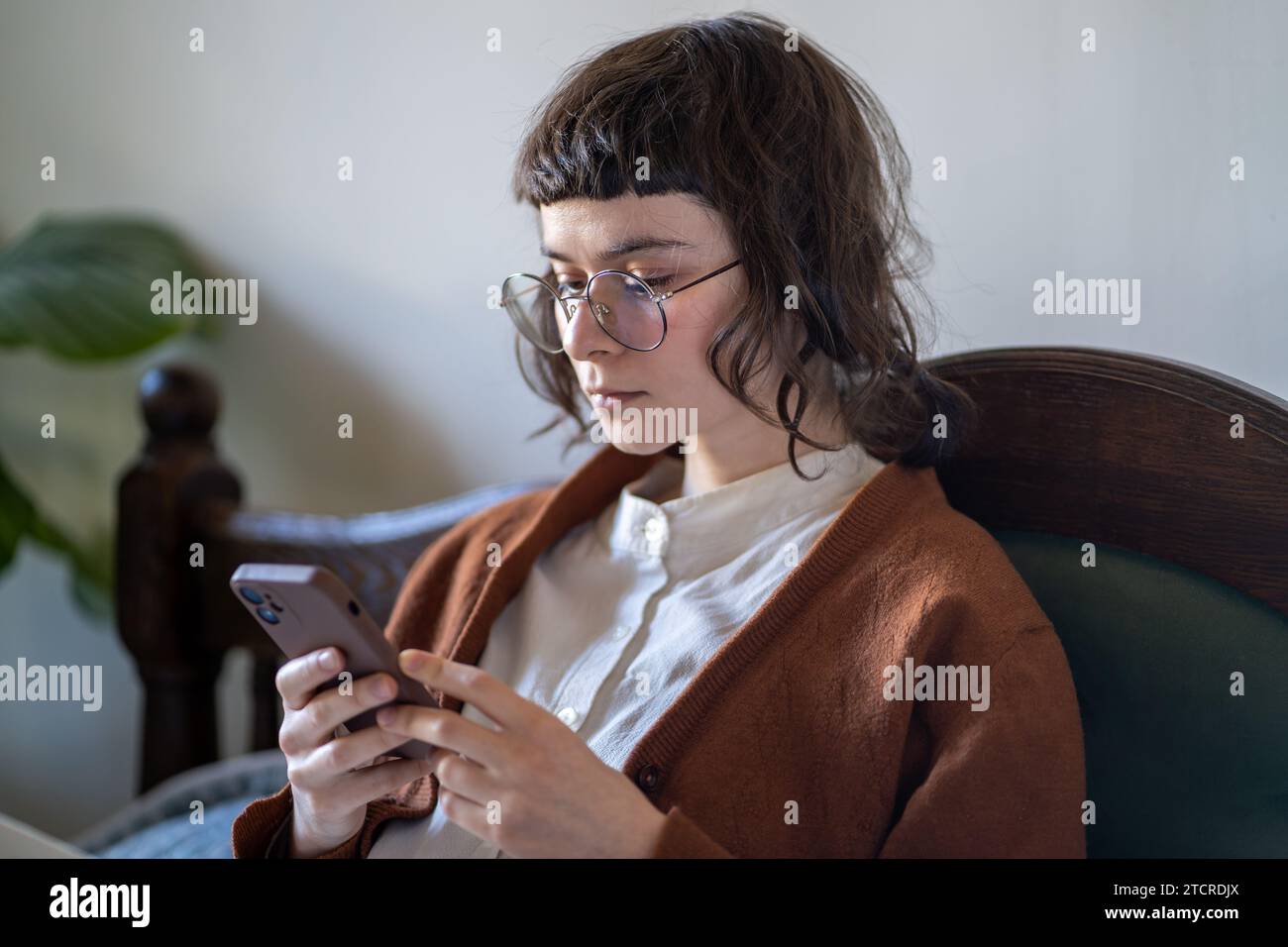 Ragazza hipster pensiva con occhiali in stile vintage che legge le informazioni sullo schermo dello smartphone. Foto Stock