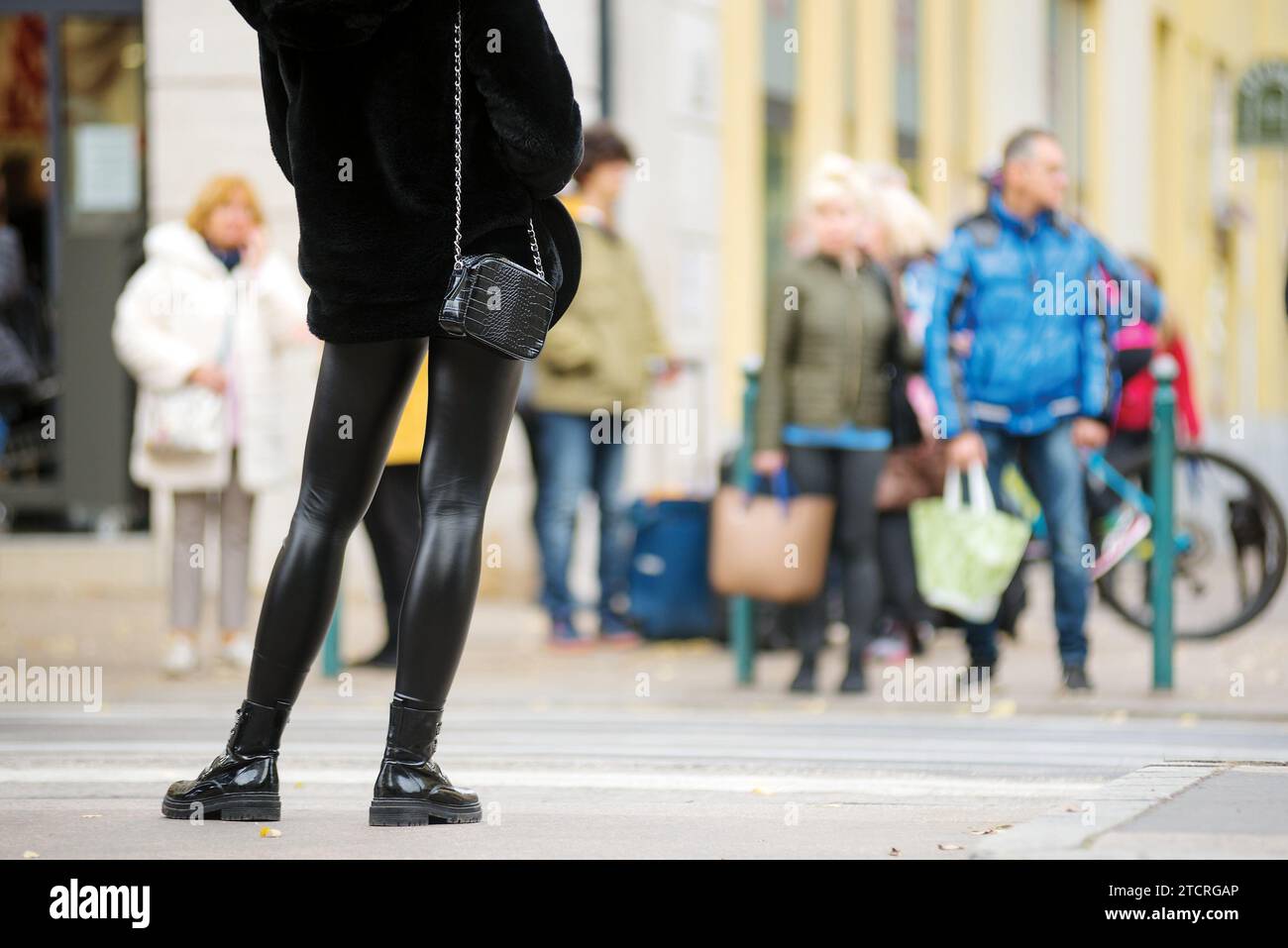 Gambe in leggings nero lucido contro una folla all'incrocio Foto Stock