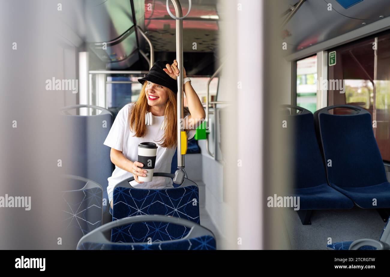 Giovane donna elegante sorride all'interno dell'autobus, abbracciando lo stile di vita urbano. Gioie per gli spostamenti in città. Foto Stock