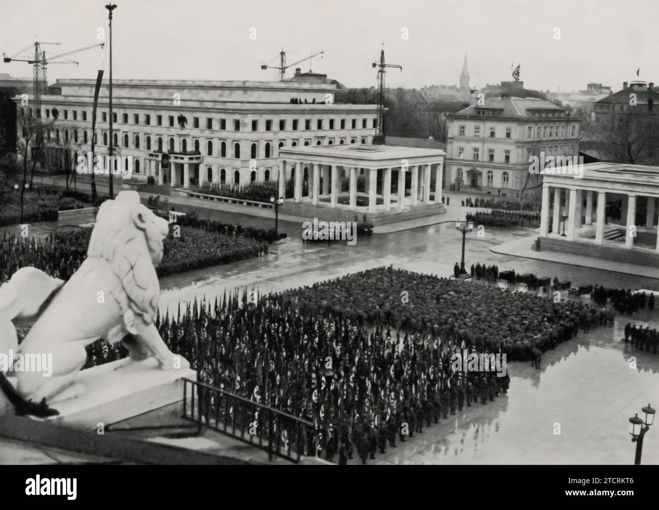 Il 9 novembre 1935, le formazioni del Partito Nazionalsocialista sono riunite sul quasi completato Königsplatz. Questa immagine cattura Adolf Hitler supervisionando l'evento, in piedi nella sua auto a tetto aperto e salutando. La data, significativa per commemorare il Putsch della Beer Hall, e il luogo, Königsplatz, un luogo chiave per i raduni nazisti, sottolineano l'importanza di questo giorno nel calendario nazista. La presenza di Hitler e le formazioni meticolosamente organizzate riflettono l'enfasi del regime sulla disciplina, l'ordine e il potere simbolico degli incontri di massa. Foto Stock