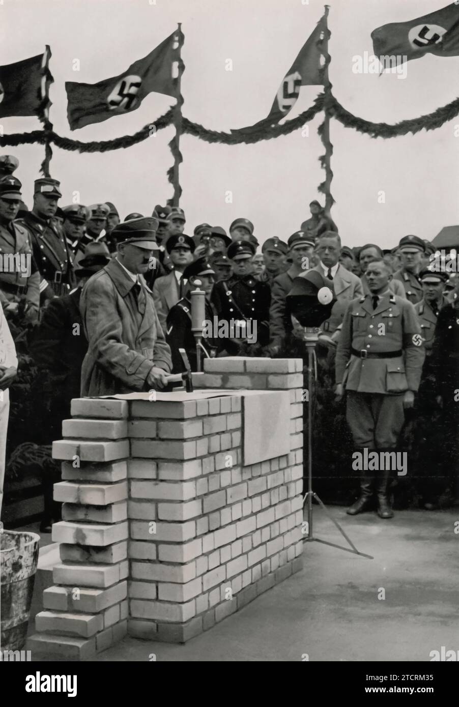 Adolf Hitler è visto mentre posa la prima pietra per la sala delle assemblee di Adolf Hitler Koog, un evento significativo che segna lo sviluppo di questa zona. Adolf Hitler Koog, parte dei progetti di bonifica e insediamento del regime, prese il nome da Hitler, simboleggiando gli sforzi nazisti nello sviluppo agrario e rurale. La cerimonia di posa della prima pietra, tipicamente un atto importante e simbolico, sottolinea l'importanza che il regime ha posto su tali progetti di costruzione, riflettendo la sua attenzione sulla rimodellatura e la coltivazione della terra come parte dei suoi più ampi obiettivi ideologici. Foto Stock