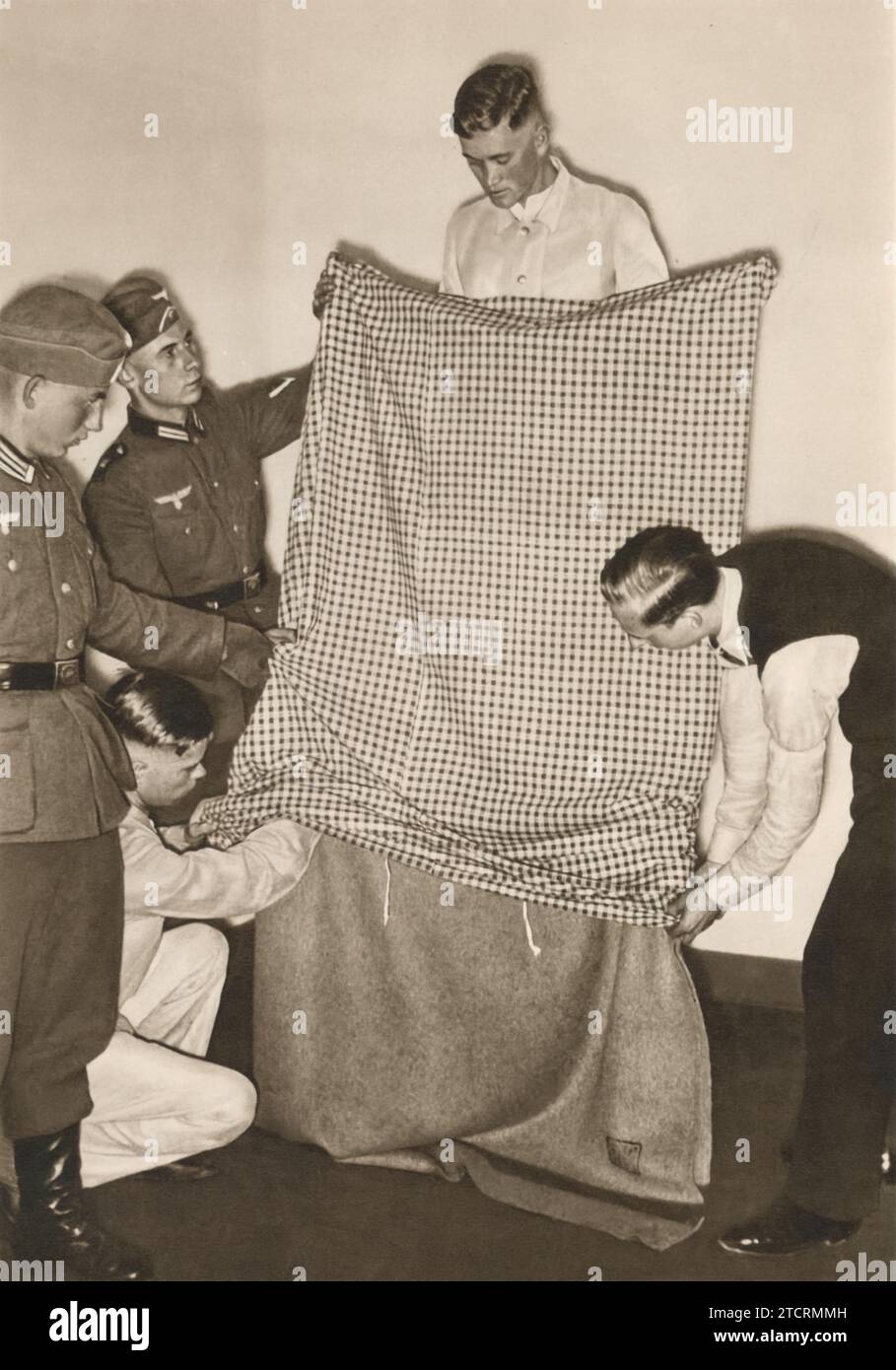 Una recluta tedesca, intorno al 1935, viene fotografata meticolosamente facendo il suo letto, un compito fondamentale nell'addestramento militare. Questo atto sottolinea l'importanza della disciplina e dell'ordine nelle forze armate, sottolineando che anche i compiti più basilari sono parte integrante della promozione di una mentalità di precisione e attenzione ai dettagli. Foto Stock