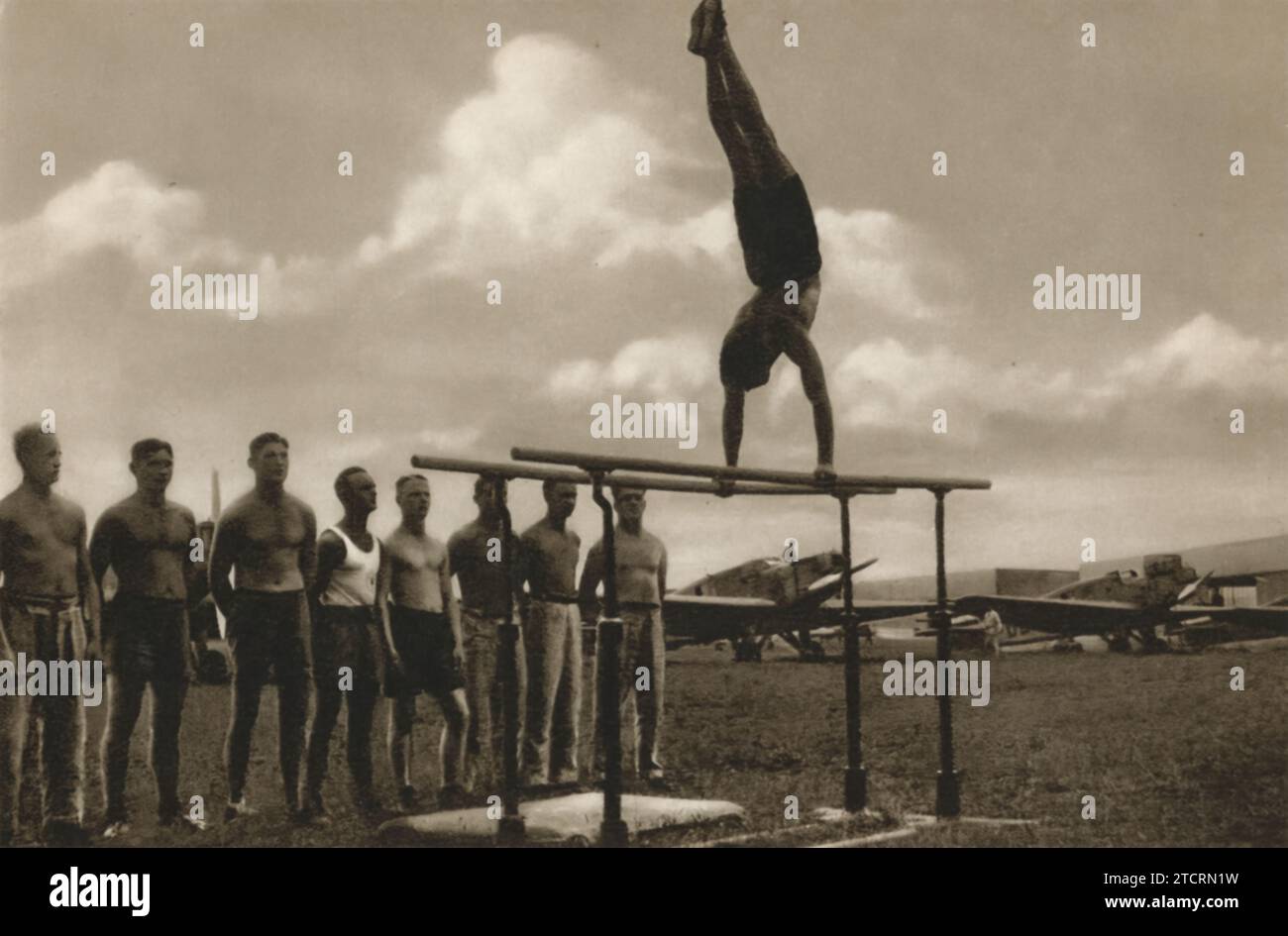 Questa immagine cattura le reclute tedesche della Luftwaffe, l'Air Force, che partecipano attivamente alla ginnastica e ad altre attività sportive. Tale allenamento fisico era una parte cruciale del loro regime, sottolineando l'importanza della forma fisica, specialmente per gli aviatori. Nell'ambiente impegnativo dei combattimenti aerei e delle manovre veloci degli aerei, la forma fisica non era solo benefica, ma essenziale. L'agilità, la forza e la resistenza sviluppate attraverso gli sport come la ginnastica hanno contribuito direttamente alla capacità delle reclute di gestire le sfide fisiche del volo. Foto Stock