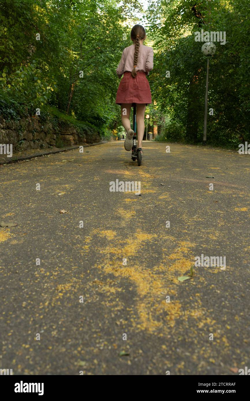 Una ragazza su uno scooter corre lungo un vicolo nel parco. Un bambino cavalca uno scooter nel parco. Ragazza su uno scooter Foto Stock
