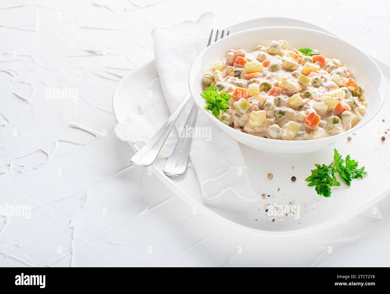 Piatto di insalata russa o insalata francese con verdure e uova condite con maionese su tavolo bianco Foto Stock