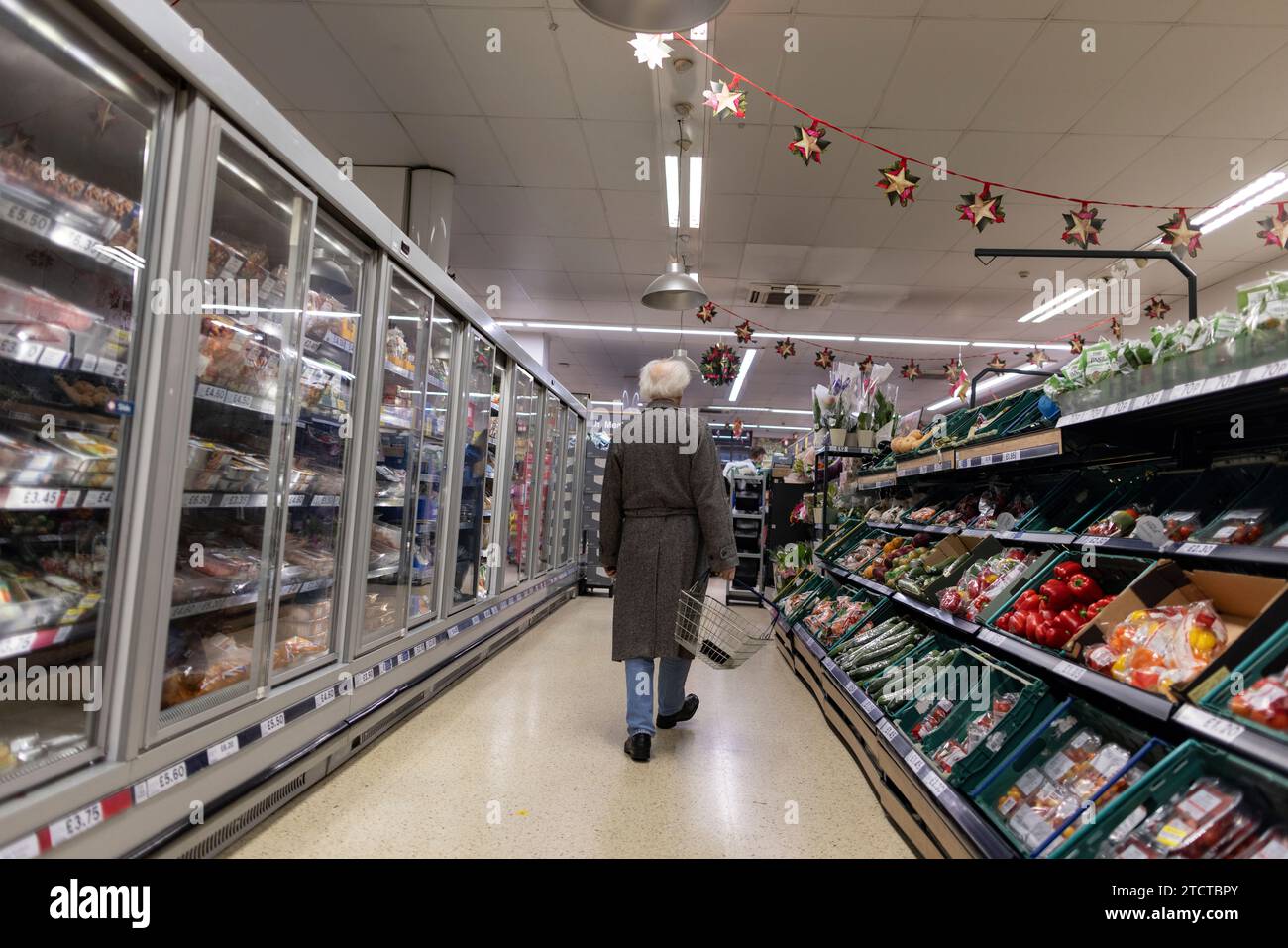 Un uomo che tiene in mano un cestino della spesa passeggia lungo la navata di un supermercato TESCO nel centro di Londra, Regno Unito Foto Stock