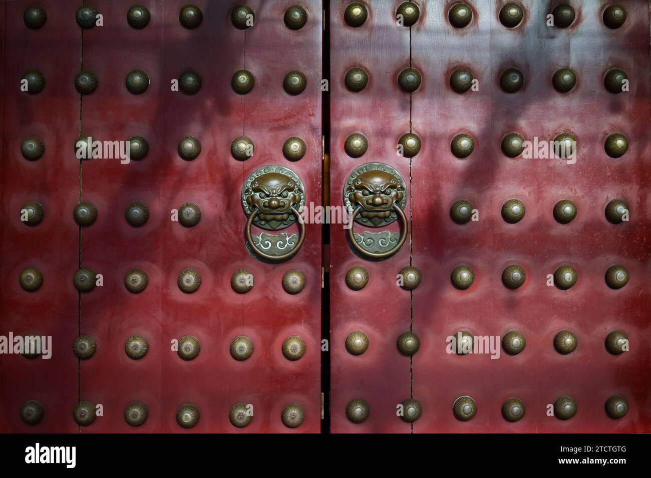 Tradizionali porte cinesi in legno rosso con battitori in ottone e borchie ornamentali. Foto Stock