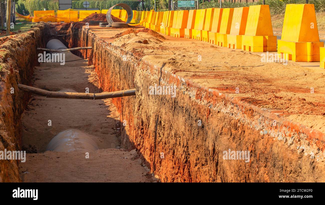 Costruzione di un nuovo layout di tubi dell'acqua in acciaio lavori di terra sotterranei scavi di trincea da vicino con vista sul progetto ingegneristico. Strada di campagna con yello Foto Stock