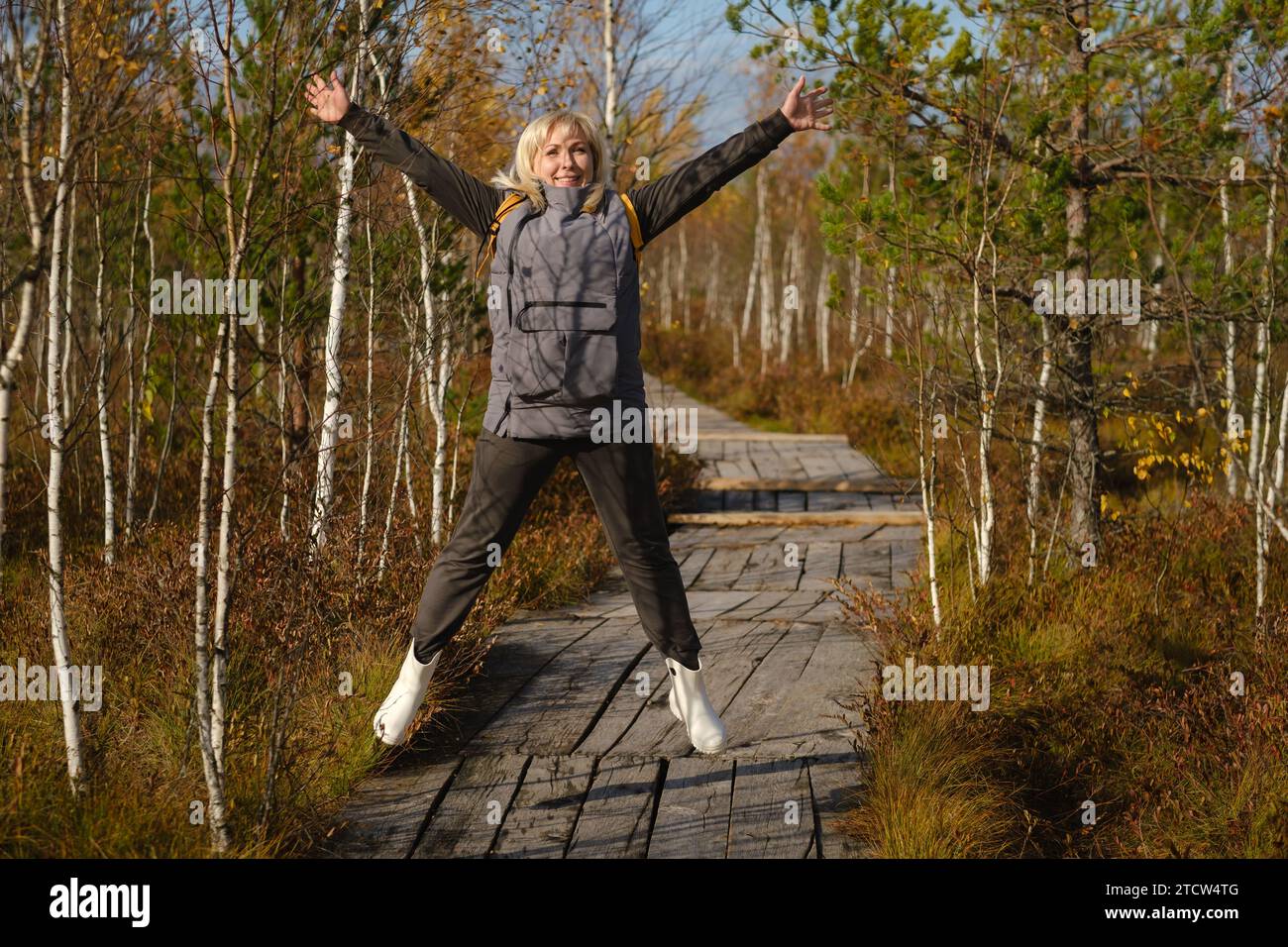 Una donna felice con uno zaino salta su un sentiero di legno in una palude a Yelnya, in Bielorussia. Foto Stock
