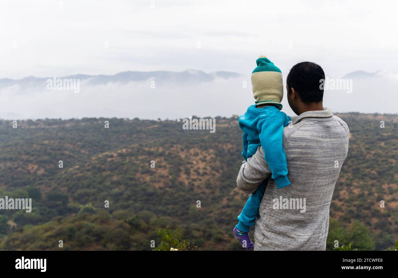 padre che tiene il figlio in braccio e gli mostra l'incredibile paesaggio montano di mattina Foto Stock