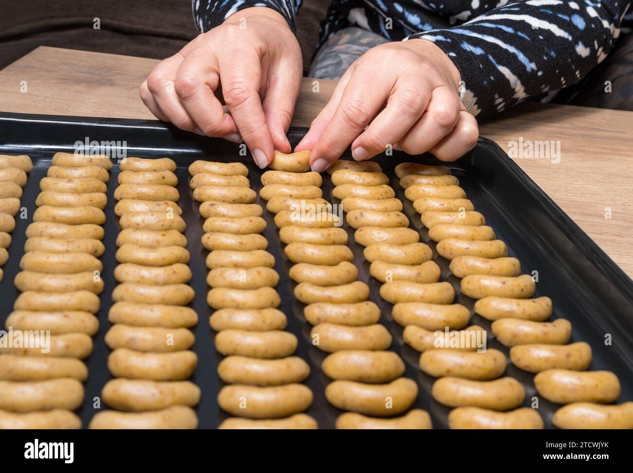 Primo piano di dolci a base di noci, panini alla vaniglia impilati a file su una griglia da forno nera Mani femminili con biscotti crudi a forma di mezzaluna della cucina ceca di Natale. Foto Stock