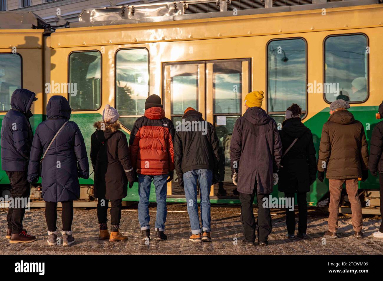 Persone che indossano abiti invernali in piedi sul marciapiede e aspettano che il tram passi a Helsinki, Finlandia Foto Stock