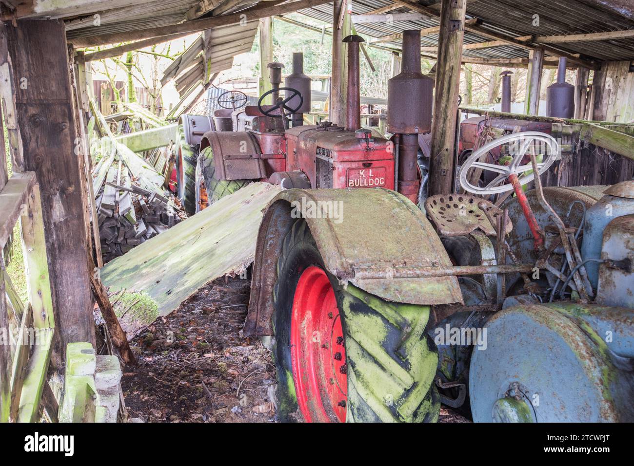 Un certo numero di vecchi trattori (Lanz Bulldog) si deteriorano mentre sono sotto copertura da un vecchio capannone/edificio esterno. Foto Stock