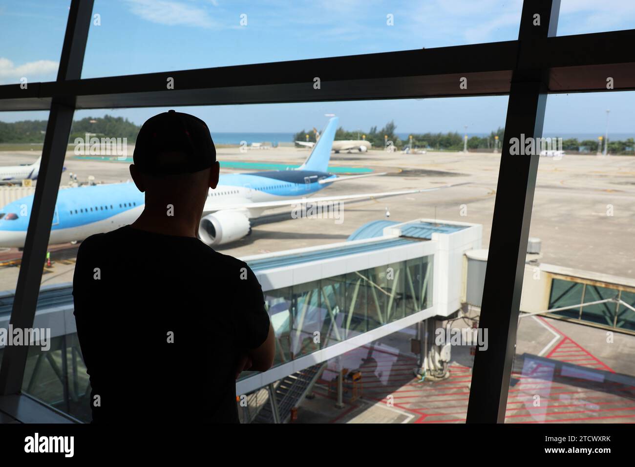 Passeggero in aeroporto, silhouette di un uomo che guarda l'aereo sull'asfalto attraverso il vetro. Vacanze e viaggi verso la costa del mare Foto Stock