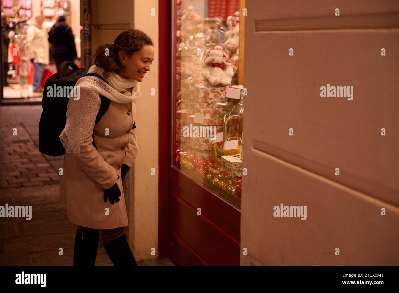Giovane donna multietnica in caldi abiti invernali, cammina in città e guarda le vetrine di Natale decorate di notte. Il concetto di vacanze di Natale A. Foto Stock