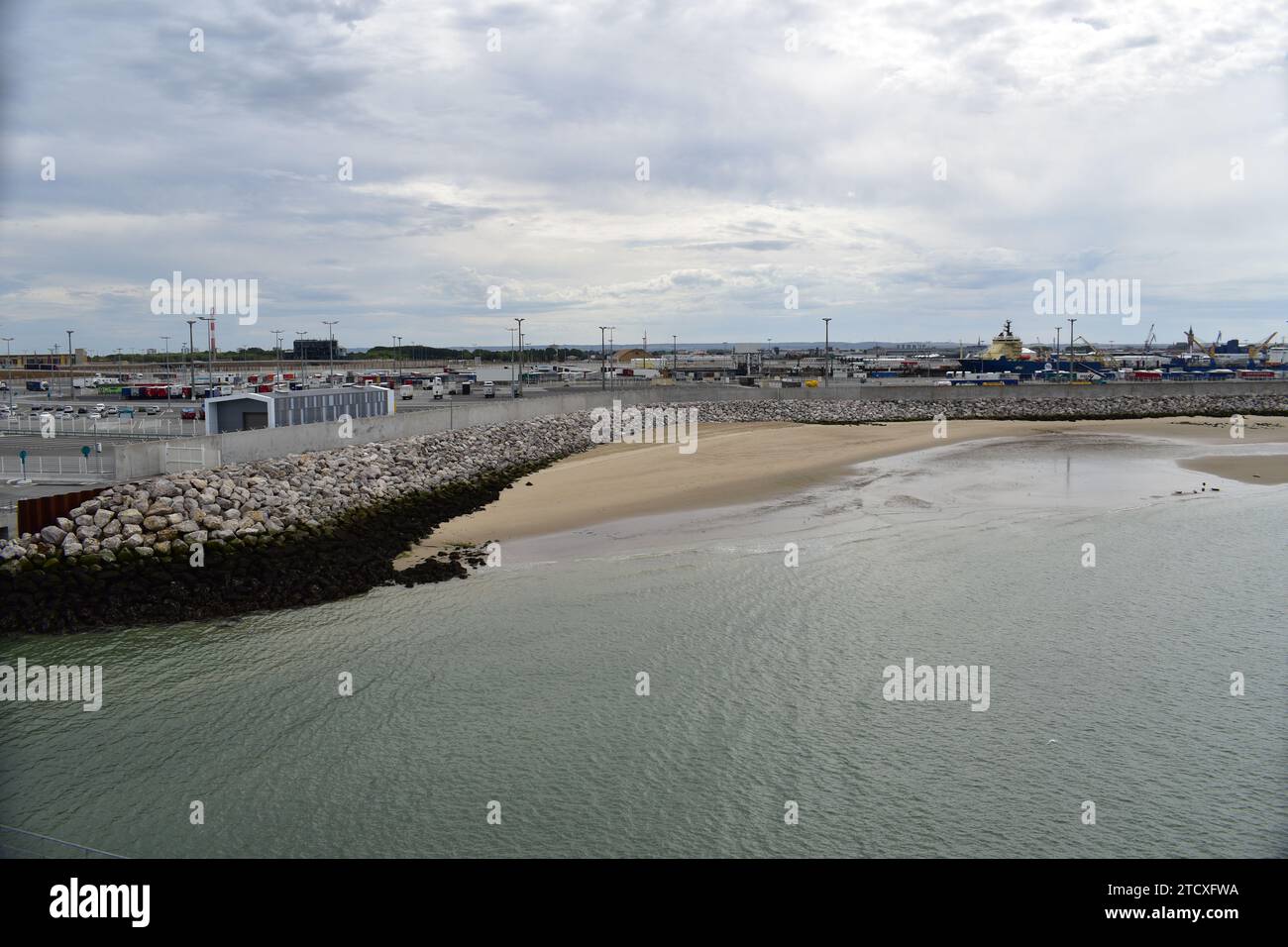 Una piccola spiaggia di sabbia di fronte al molo in cemento protetto da massi di pietra nel porto dei traghetti di Calais Foto Stock