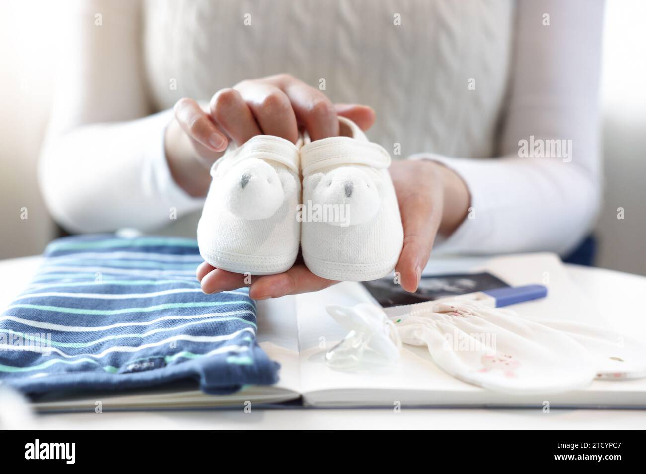 Una donna incinta sta tenendo in mano e mostrando le sue scarpe da bambino, davanti ci sono i quaderni e gli oggetti per bambini Foto Stock