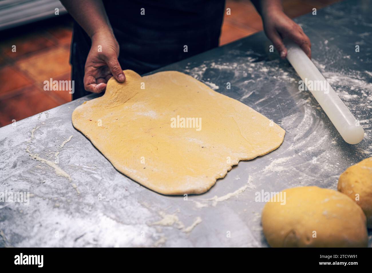Le mani delle donne fanno rotolare l'impasto nel bancone professionale della cucina Foto Stock