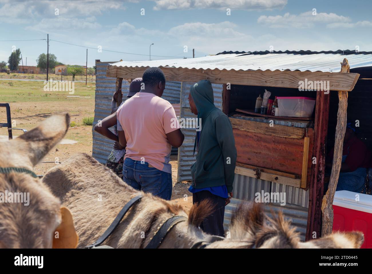 gente africana che chiacchiera davanti a una baracca nel villaggio, carrello degli asini parcheggiato di fronte Foto Stock