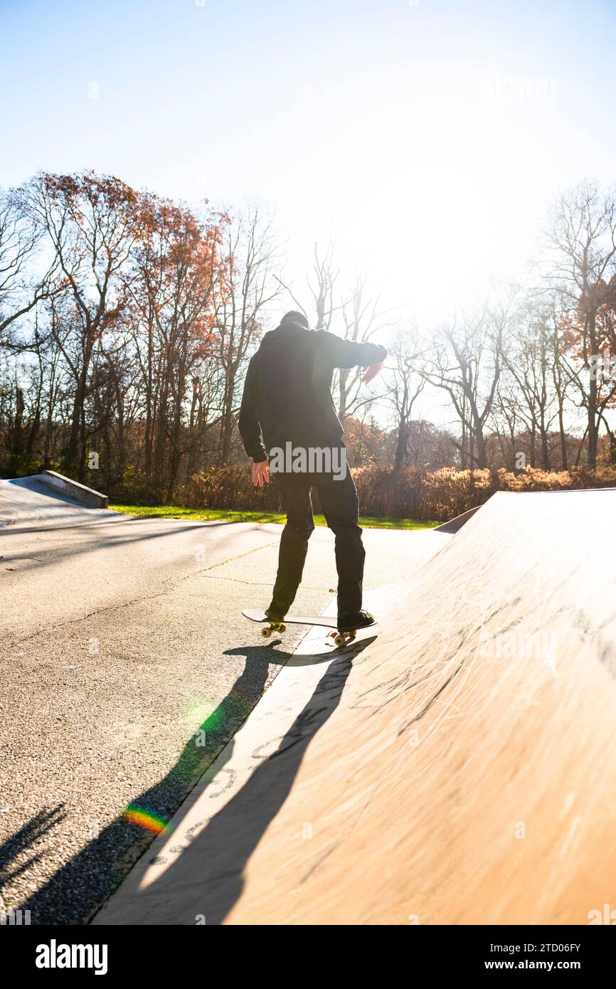 Solo Man skateboard su una rampa per skatepark in autunno con il bagliore delle lenti Foto Stock