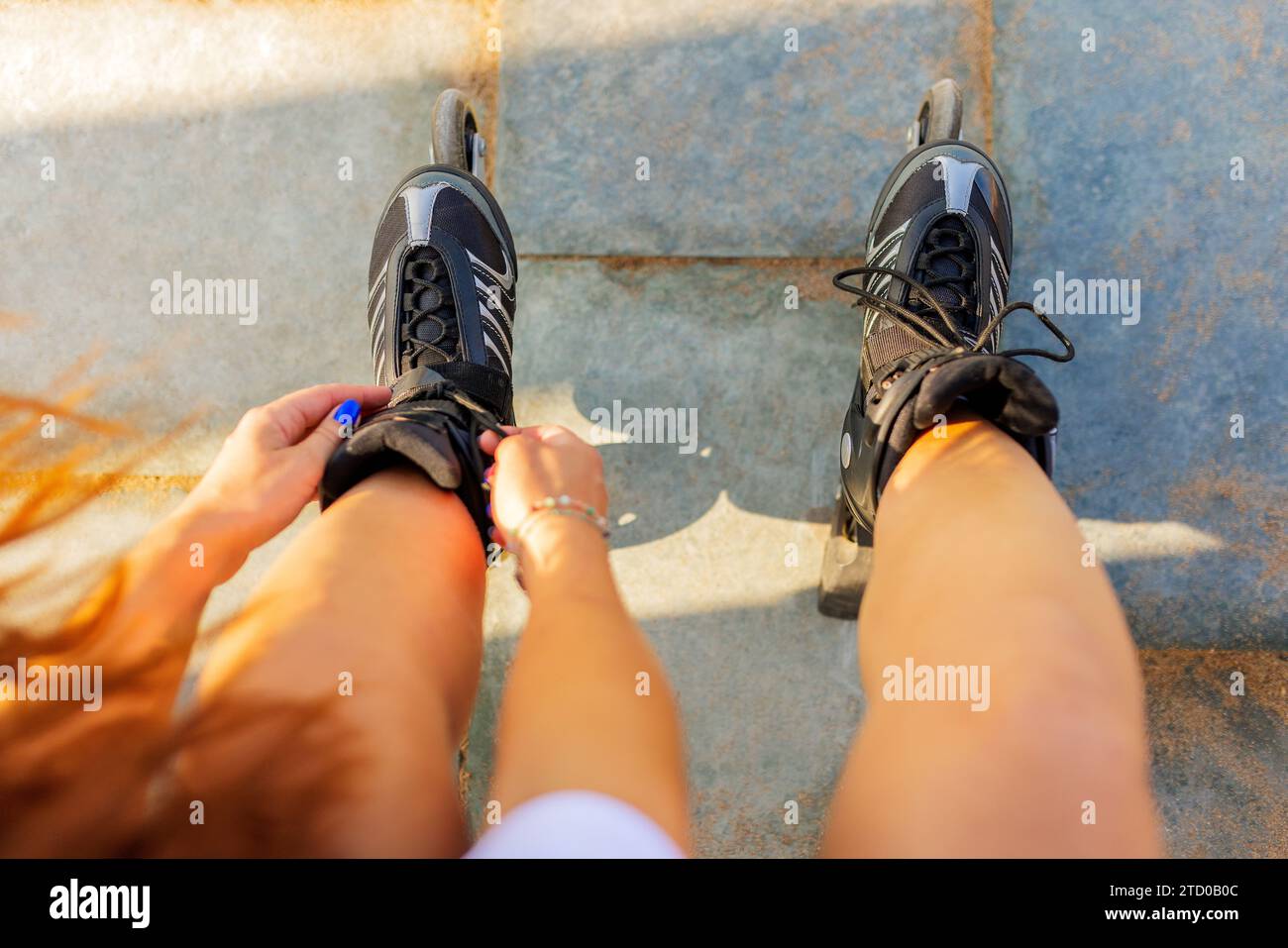 Ritaglio ad angolo elevato di donna anonima che lega pizzi di pattini a rotelle neri in linea sul sentiero nel parco Foto Stock