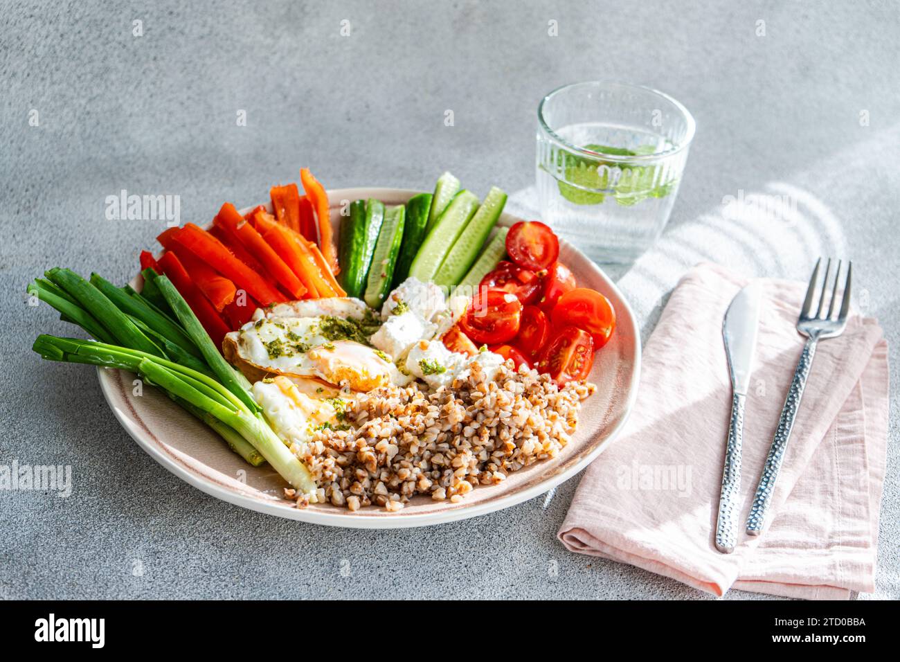 Un piatto per la colazione fresco e salutare con una varietà di verdure crude, feta cremosa, grano saraceno sano e uova fritte, il tutto condito con pesto Foto Stock