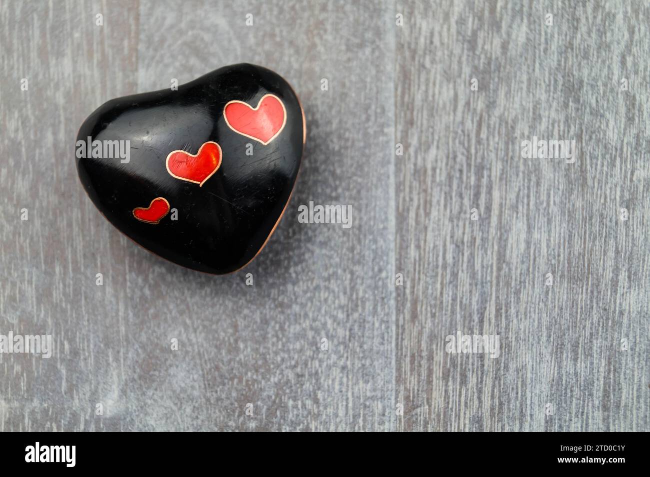 cuore nero con piccoli cuori rossi su legno Foto Stock