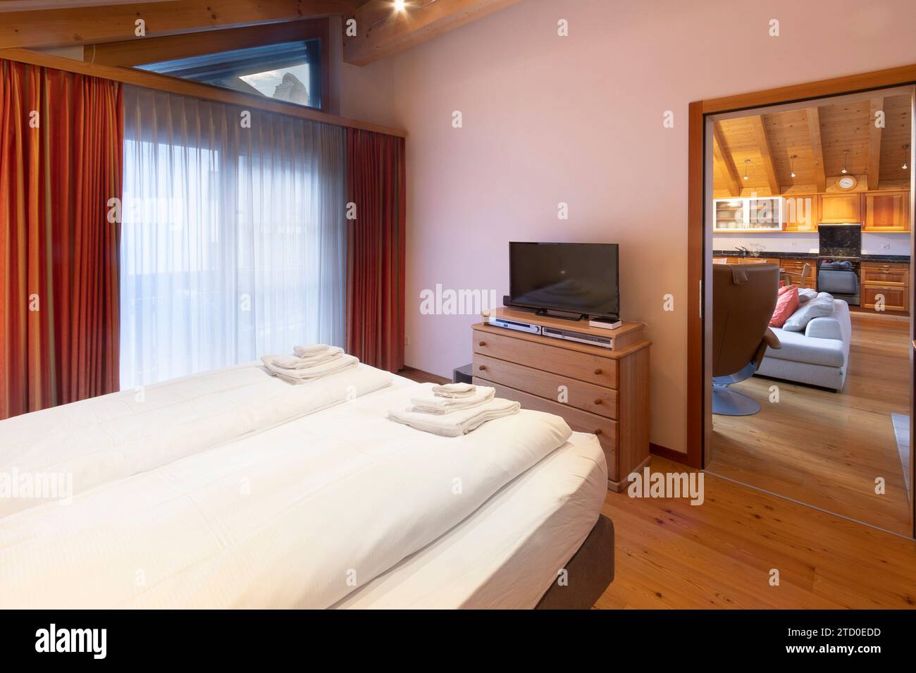 Una camera da letto calda e invitante con un grande letto con lenzuola fresche, mobili in legno e un picco nell'area soggiorno adiacente con angolo cottura Foto Stock