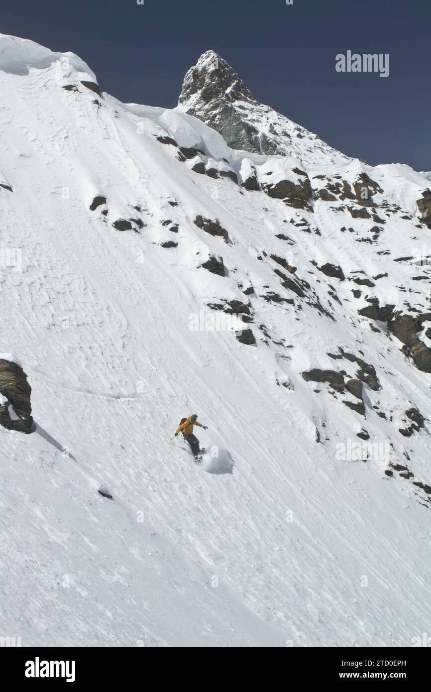 Angolo elevato di persona anonima con zaino che scende durante lo snowboard su una pista innevata di montagna contro il cielo blu durante le vacanze allo Swiss al Foto Stock